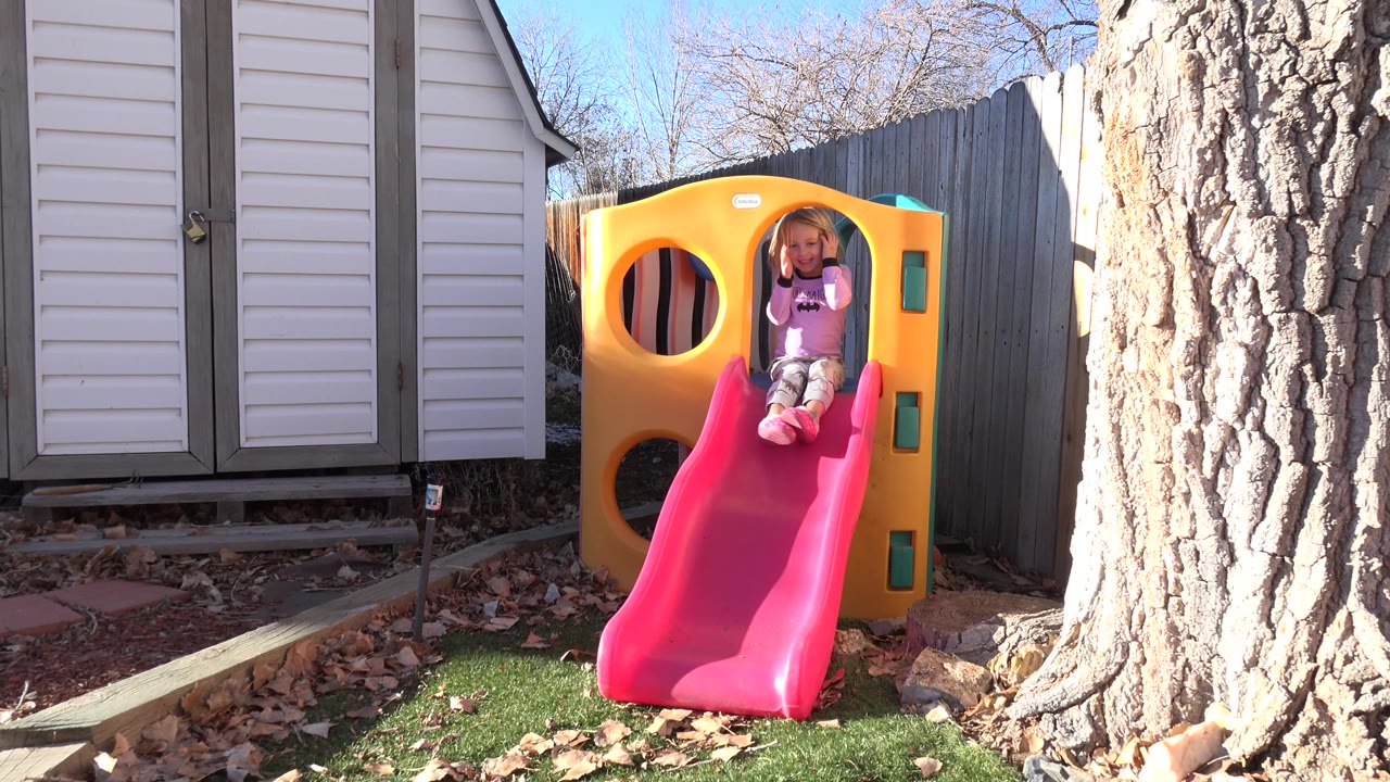Young girl seated at the top of a red slide beside a yellow play structure.