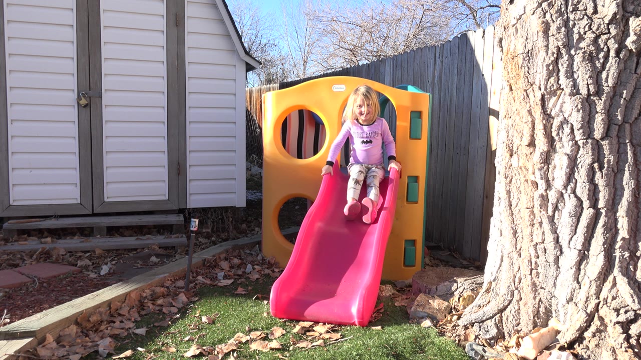 Young girl sitting at the top of a red backyard slide.