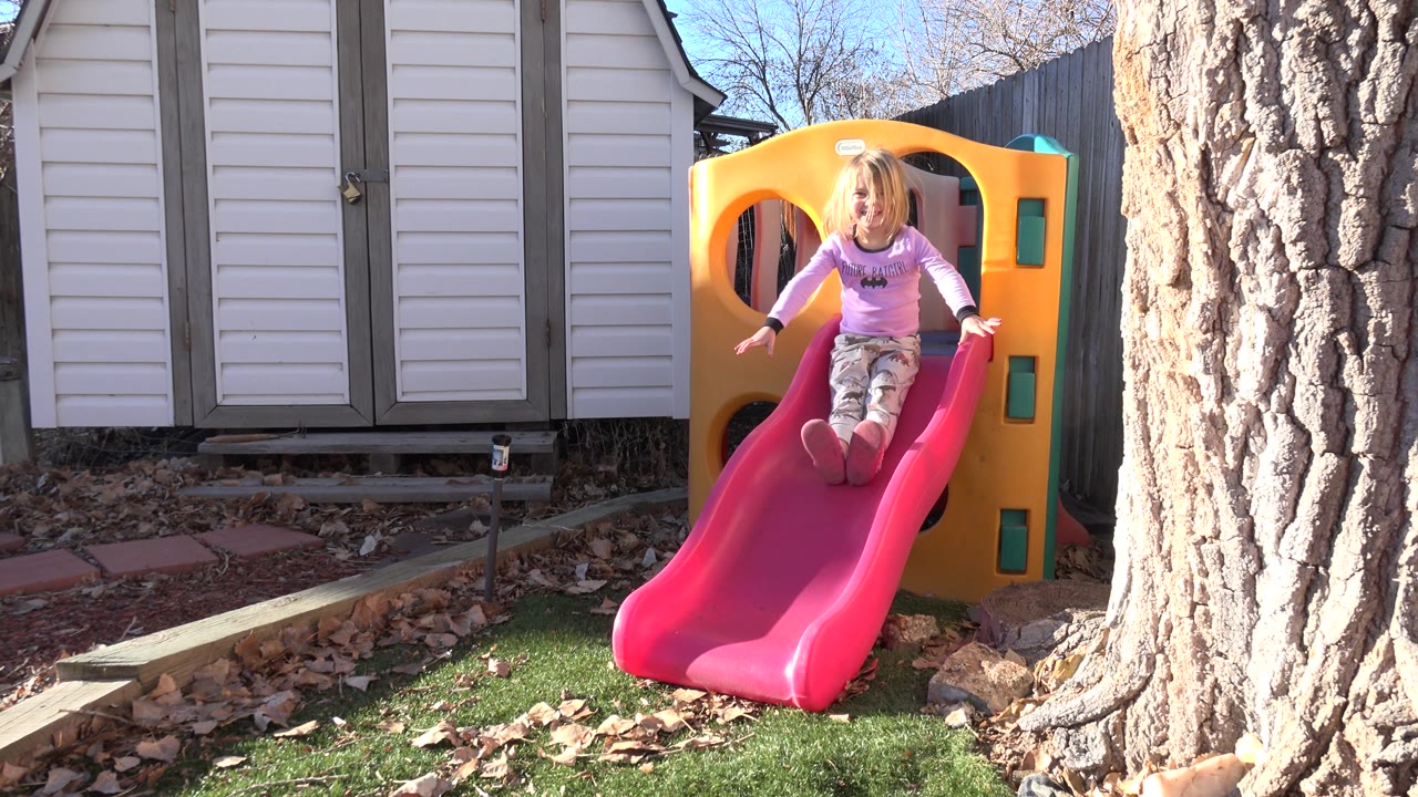 Young girl sliding with arms out on the red slide.