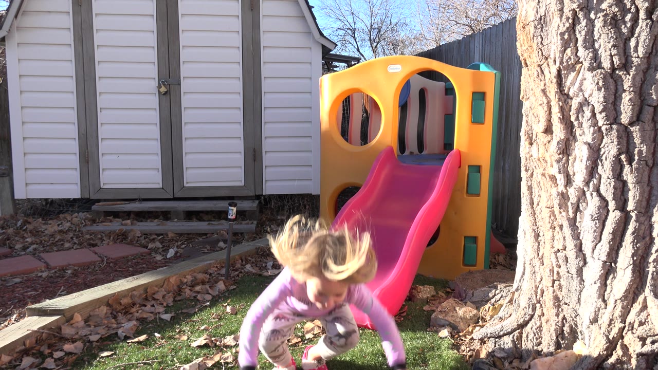 Blond child entering the foreground near a backyard slide.