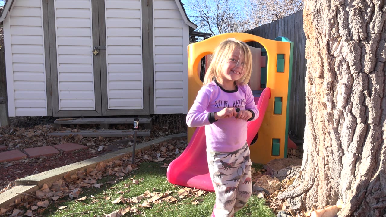 Young girl in a pink shirt standing near a red slide and yellow playhouse.