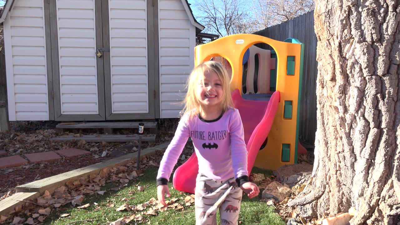 Young girl smiling near a red slide and yellow playhouse in a backyard.