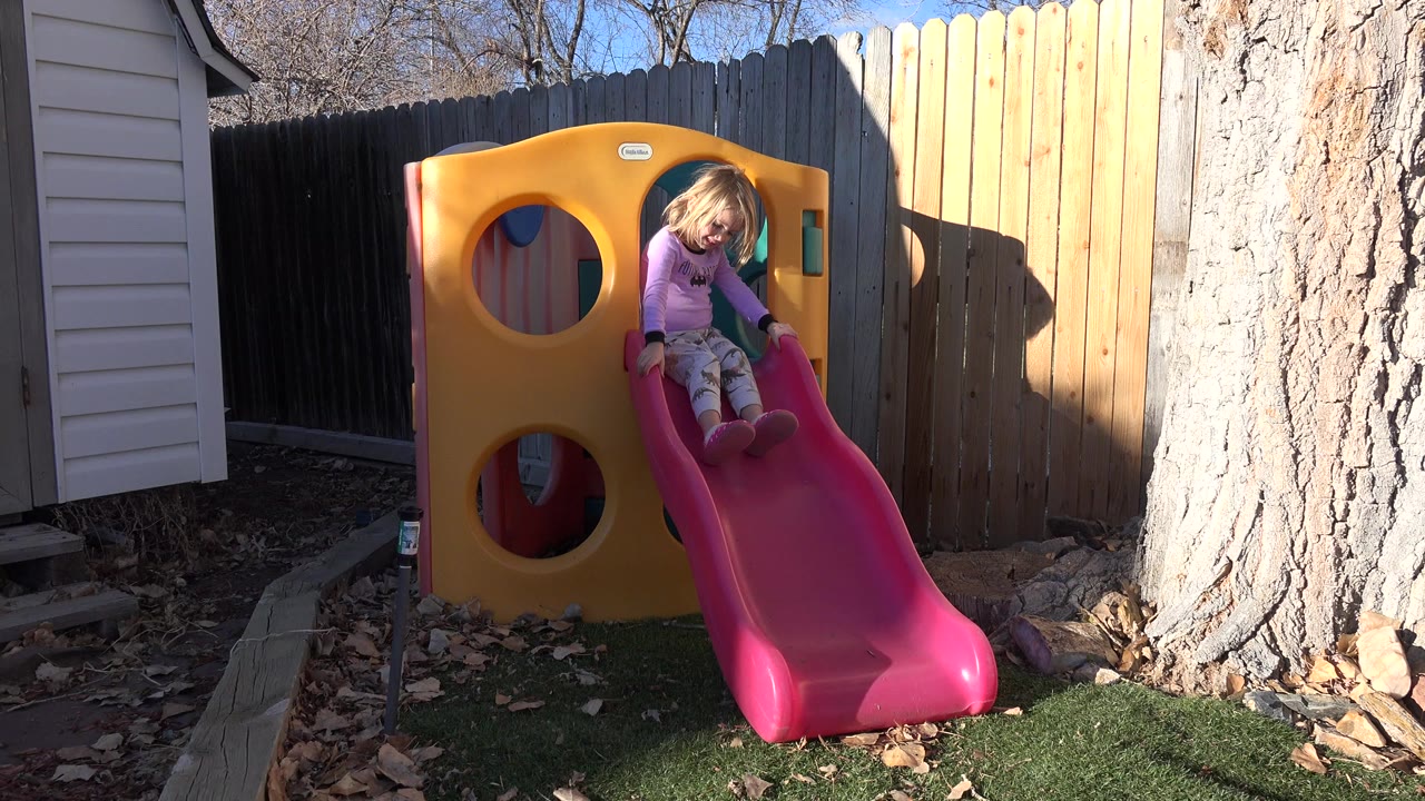 Young girl sits near the top of a pink backyard slide.