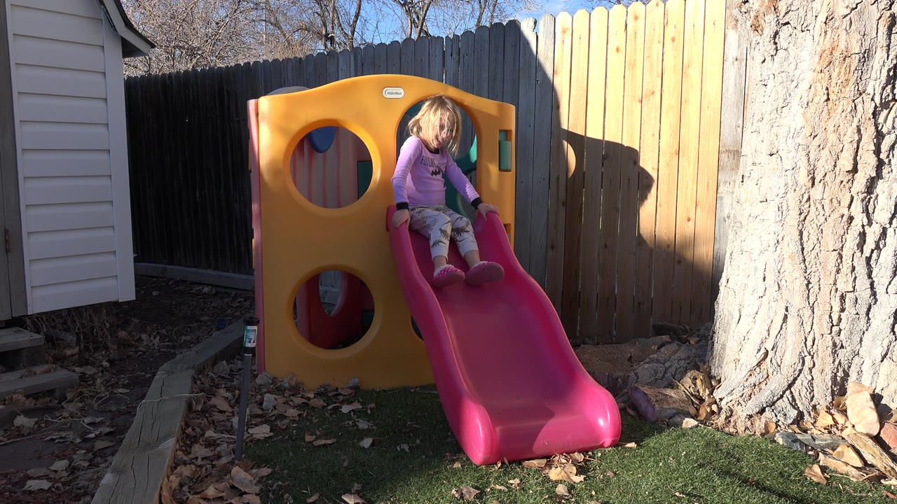 Young girl sitting at the top of a pink backyard slide.