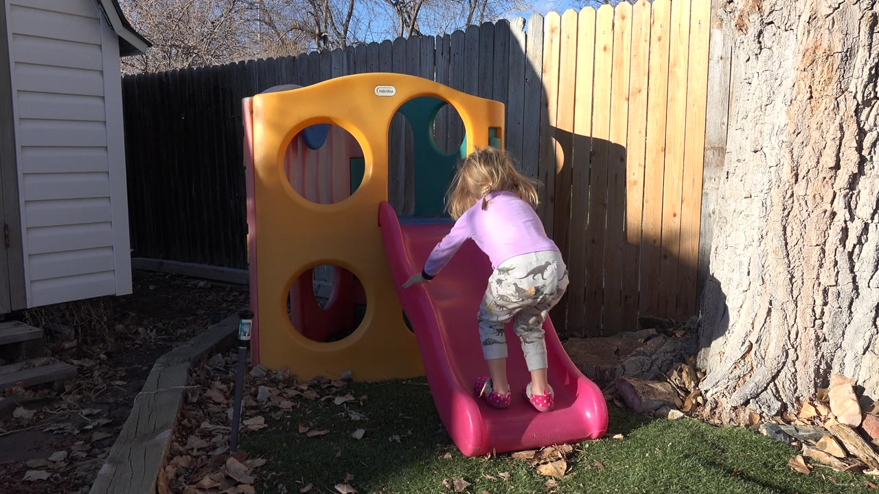 Toddler starts climbing a pink backyard slide.