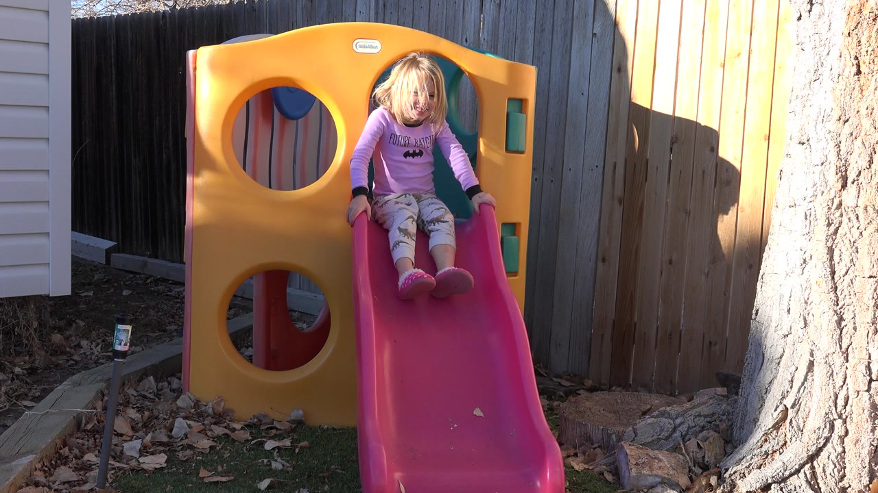 Young girl seated at the top of a pink backyard slide.