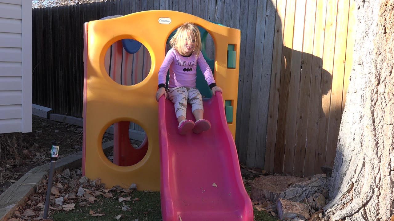 Girl continues down the backyard slide in sunlight.