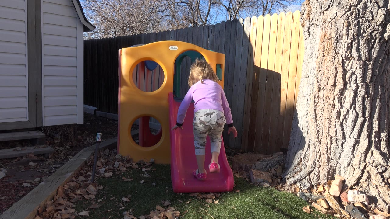 Young girl standing at the base of a pink backyard slide.