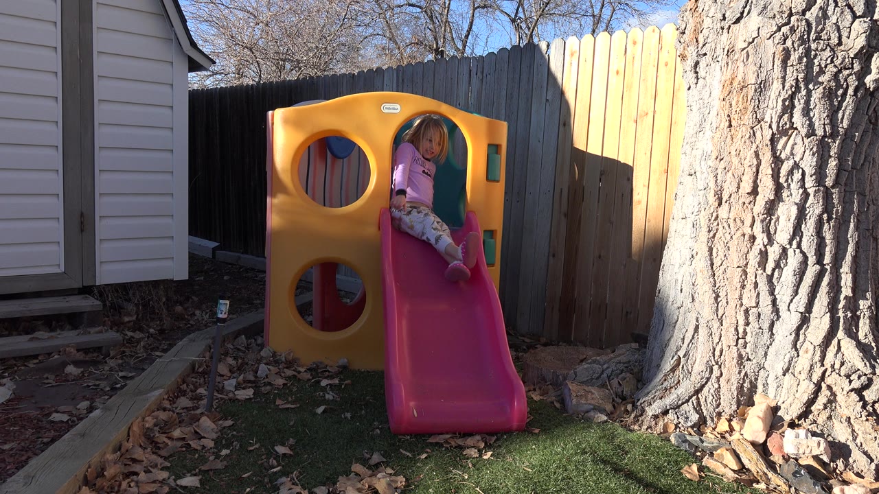 Young girl seated at the top of a pink backyard slide.