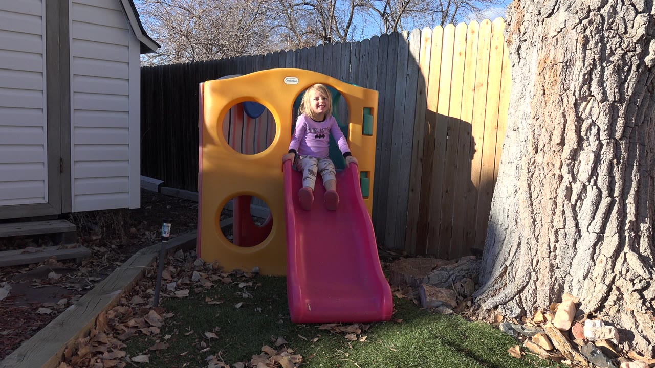 Young girl sitting at the top of a pink backyard slide.