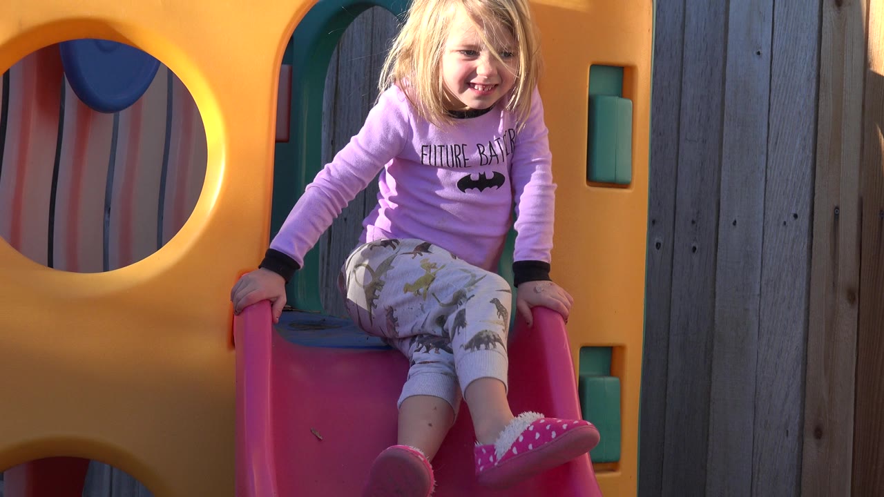 Young girl sitting at the top of a red playground slide.