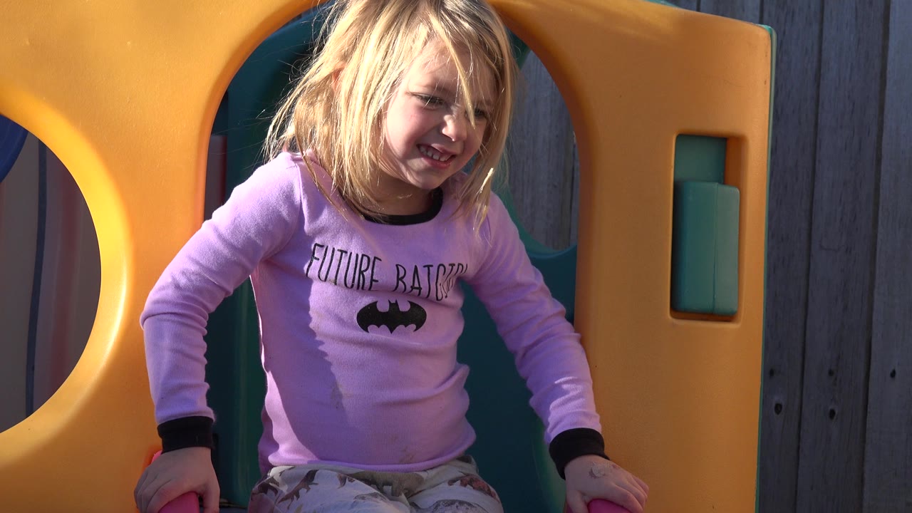 Blond girl in a purple shirt standing in a yellow playground opening.