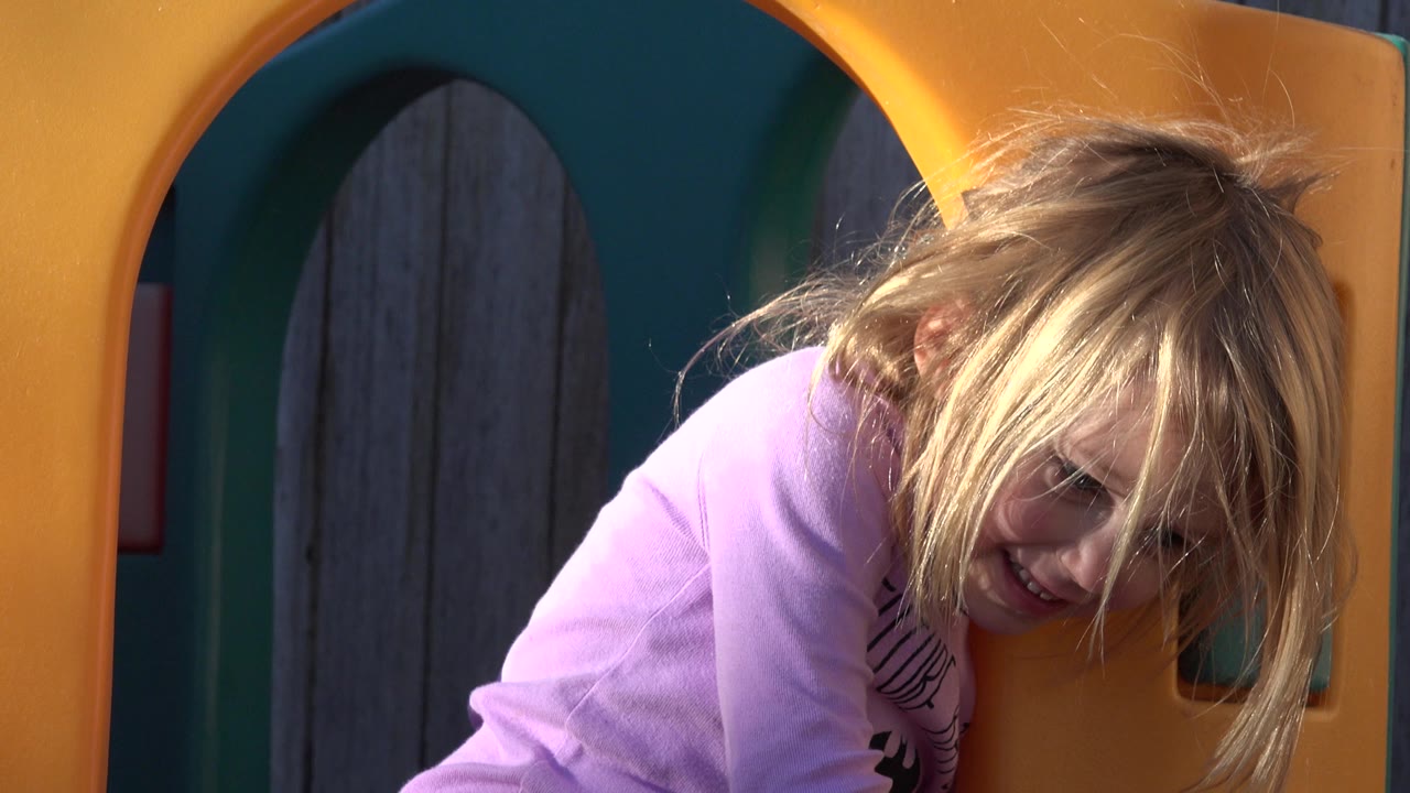 Blond girl leaning through a yellow play structure opening.