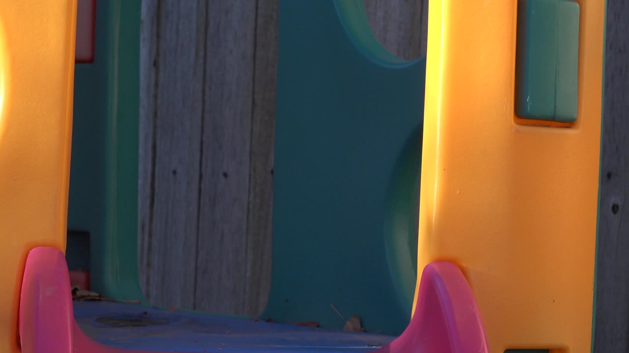 Tight Westminster, Colorado backyard frame showing the yellow playset wall, teal plastic panel, wood fence boards, and red slide edge with no visible people.
