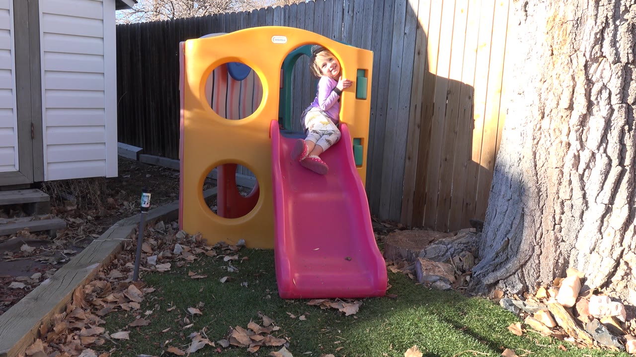 Young girl at the top of a pink slide beside a yellow play structure.