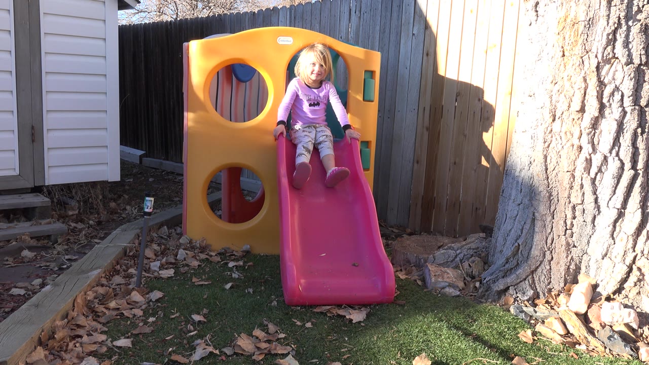 Young blond girl seated at the top of a pink backyard slide