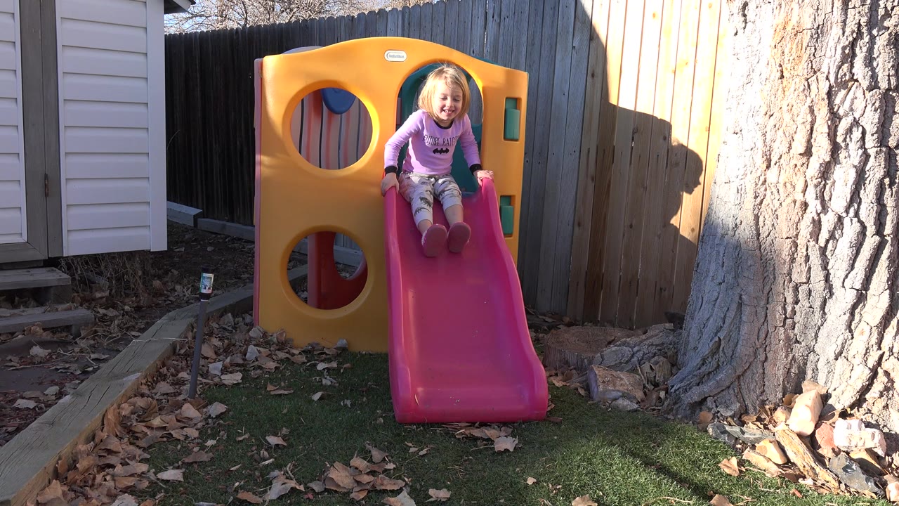 Young girl seated at the top of a pink backyard slide.