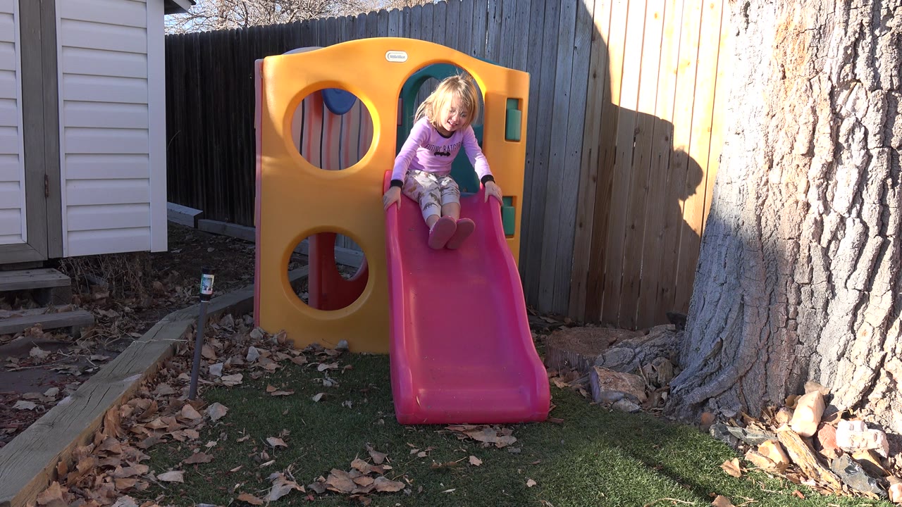 Young girl sitting at the top of a red slide on a yellow playhouse.