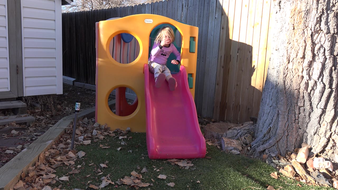 Young blonde girl sitting at the top of a pink backyard slide.