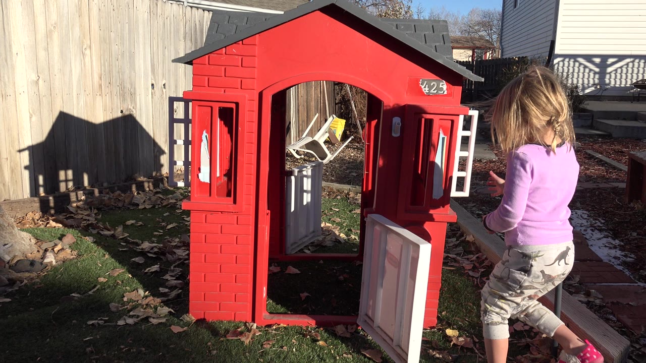 Young girl approaches a red backyard playhouse with open doors.