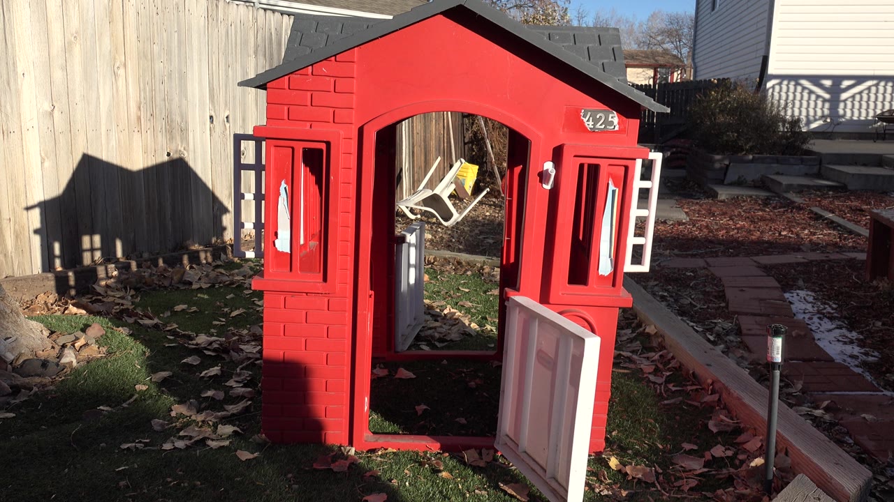 Open red playhouse with white door and yard path.