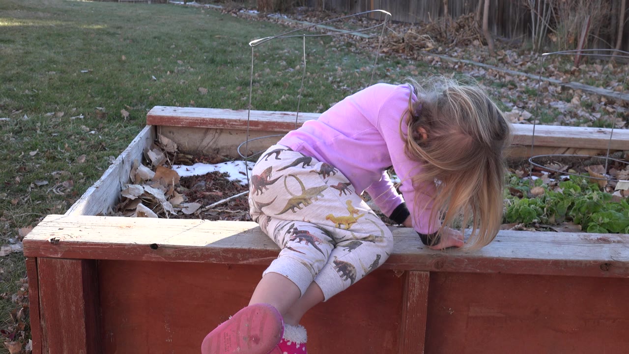 Young girl in pink pajamas leans over a raised flower bed.