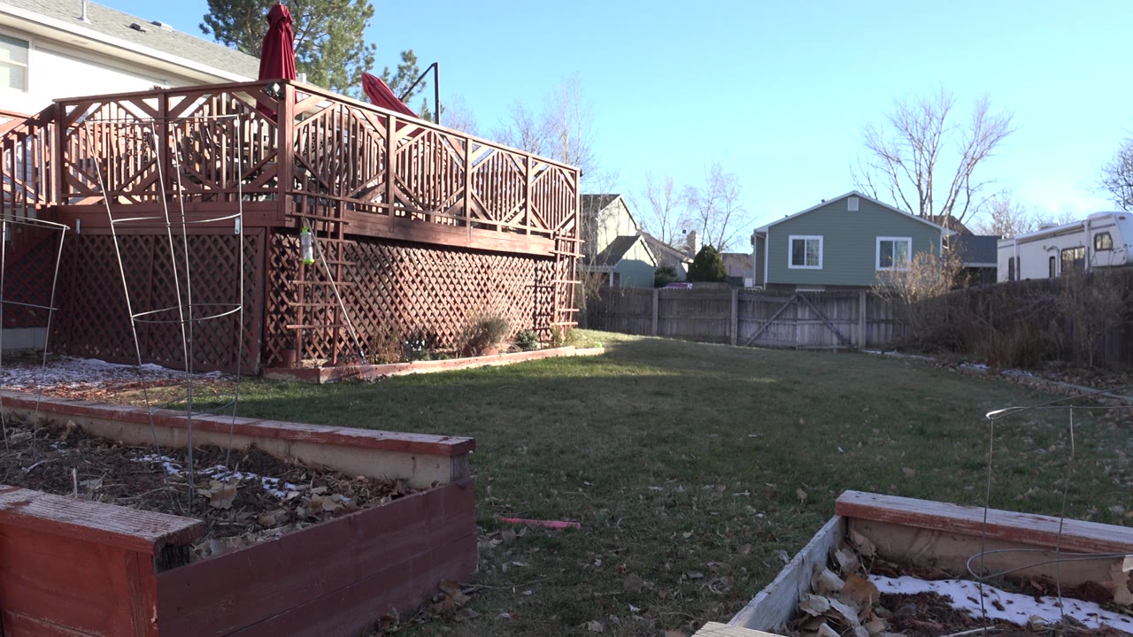 Suburban backyard with wooden deck, lawn, and raised garden beds.