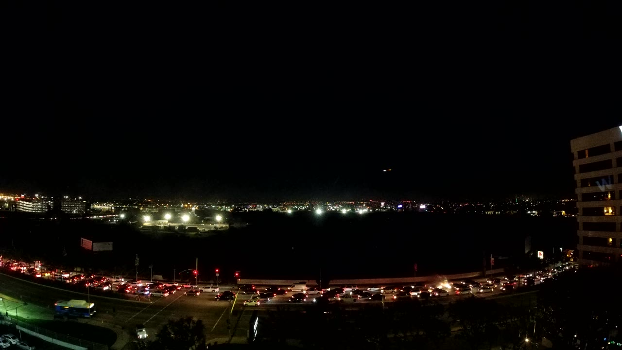 Los Angeles night traffic continues across the lower frame, with clustered red taillights, bright horizon lights, a dark open center, and no visible people.