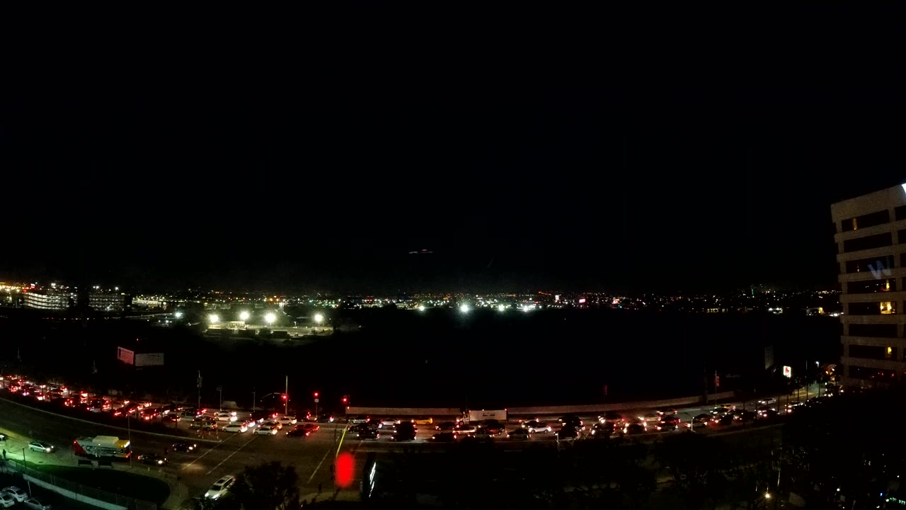 Los Angeles nighttime traffic fills the lower frame with red taillight streaks, bright road lighting, a vertical building edge at right, and no visible people.
