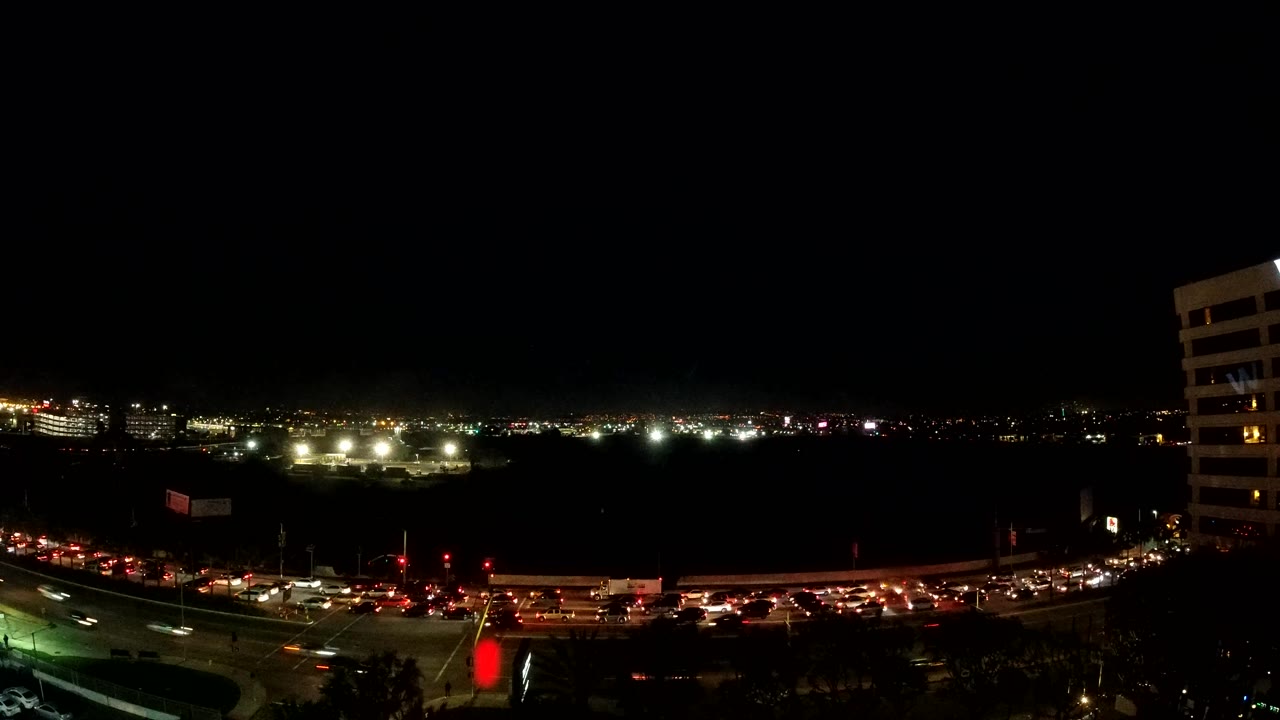 Los Angeles road traffic forms bright red and white lines across the bottom of the frame, with a dark open area in the middle distance and no visible people.