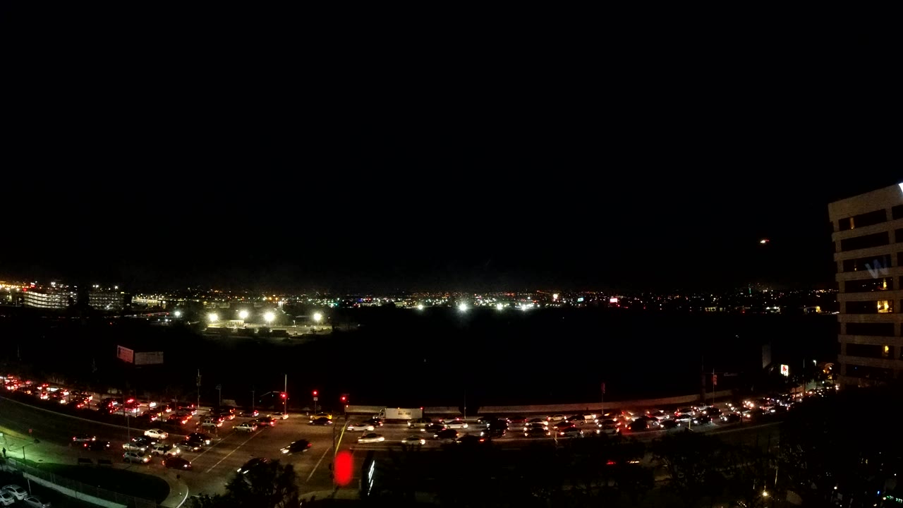 A wide Los Angeles night frame shows heavy traffic curving through the foreground, small distant lights across the horizon, a dark sky, and no visible people.