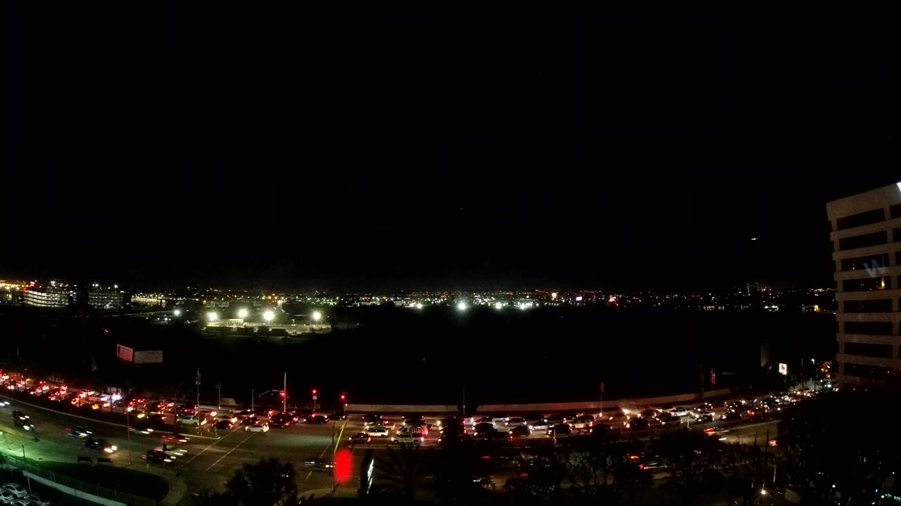Elevated nighttime view in Los Angeles with streams of car lights across a wide avenue, distant city lights, a dark open midground, and no visible people.