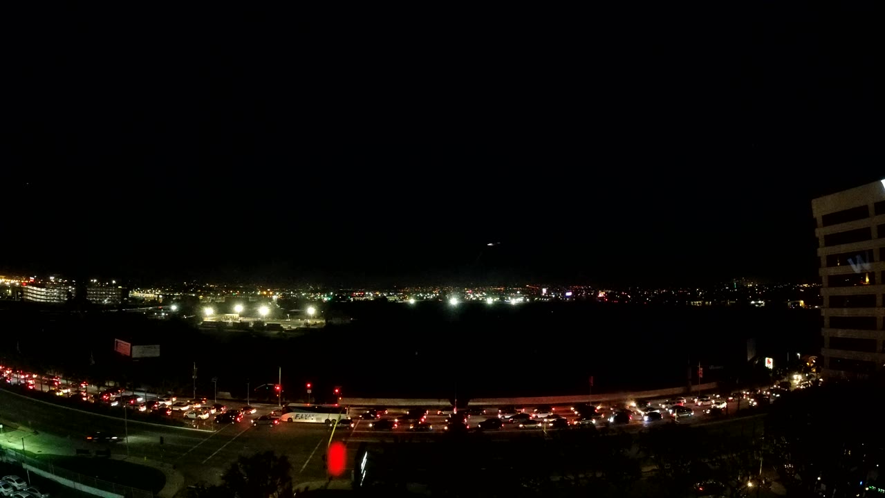 Mid-early frame of Los Angeles road traffic at night, with a dark open middle area, a line of vehicle lights near the bottom, and no visible people.