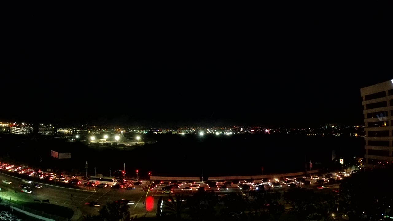 Nighttime Los Angeles traffic passing through a lit intersection.
