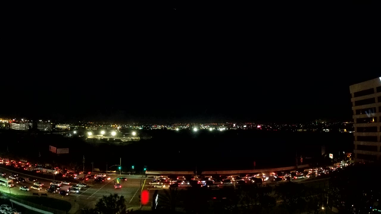 Elevated night view of Los Angeles traffic with red tail lights and white headlights along a busy road, a dark horizon, and no visible people.