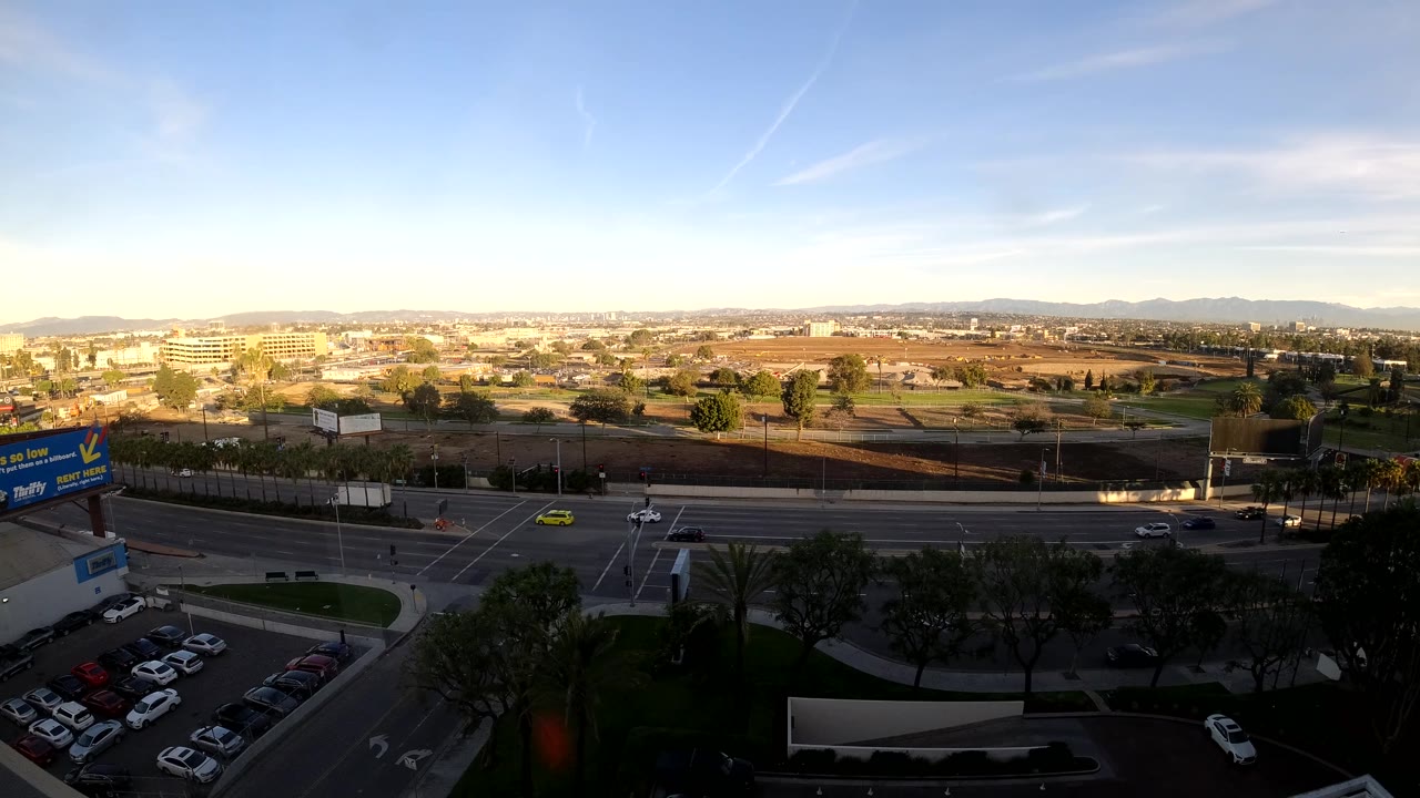 Sunset traffic passes below an elevated view of parking lots and city blocks.