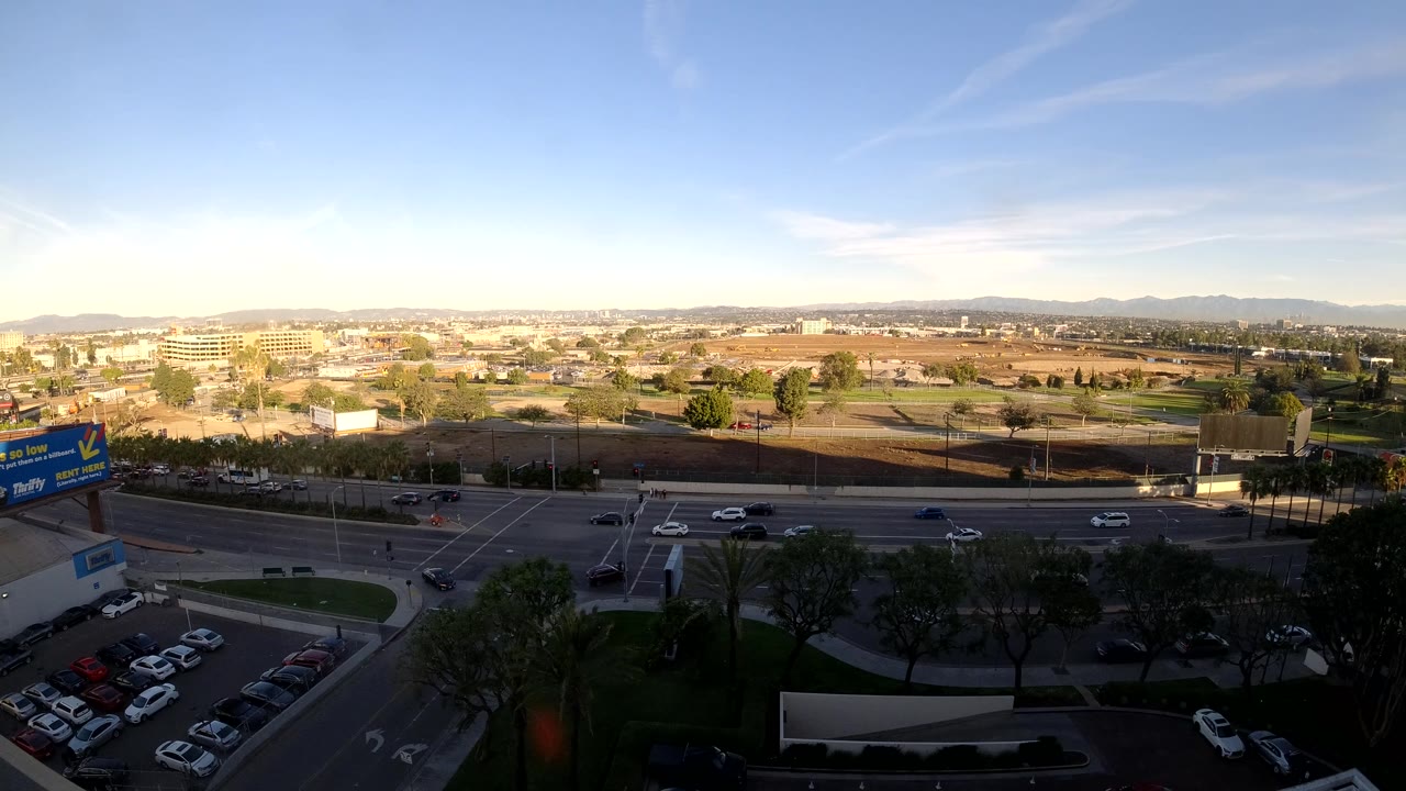 High view over road traffic, parking area, trees, and distant urban hills