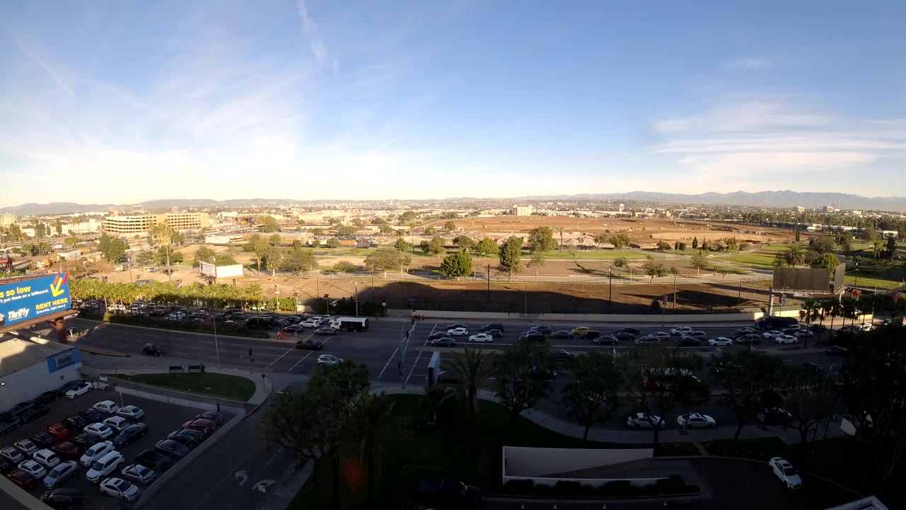 Cars and trucks move through a wide intersection area under bright sky.