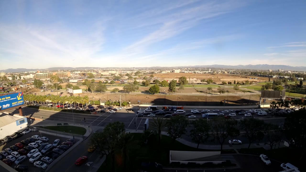 High wide view of a Los Angeles road corridor with parking lots and low buildings beyond.