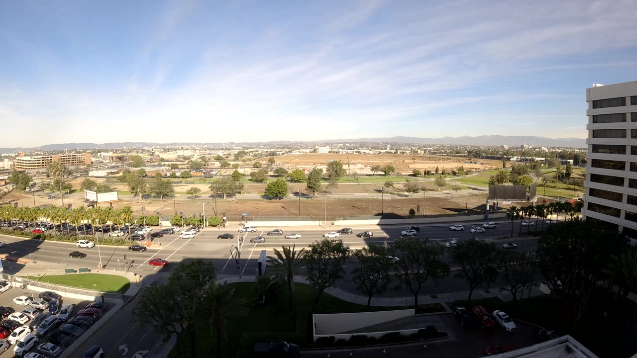 Wide urban view with cars moving along a sunlit road and shaded trees below.