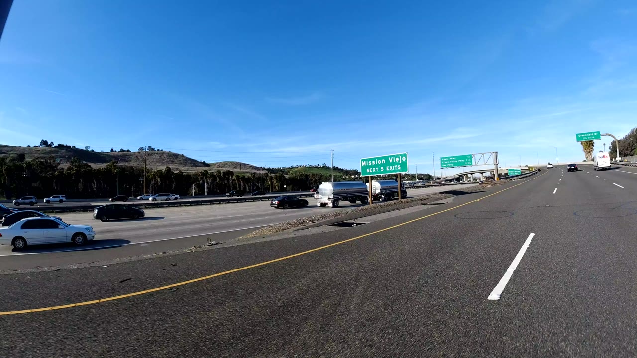 Wide freeway view in Orange, California with green exit signs, cars on multiple lanes, hillside background, bright daylight, and no visible people.
