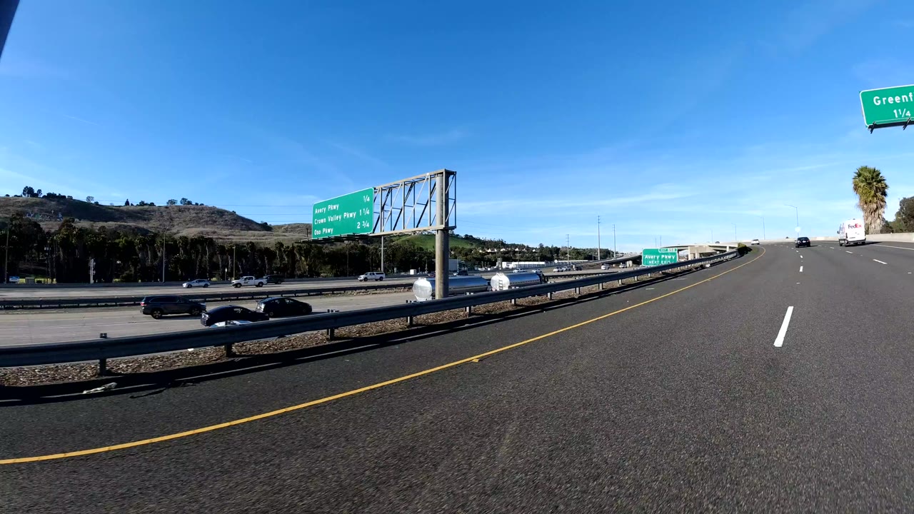 Roadway lanes beside a guardrail with cars and green freeway signs ahead.
