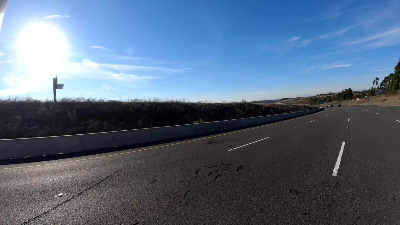 A freeway in Orange, California passes a concrete barrier and roadside sign under intense sun, with a few vehicles ahead and no visible people.