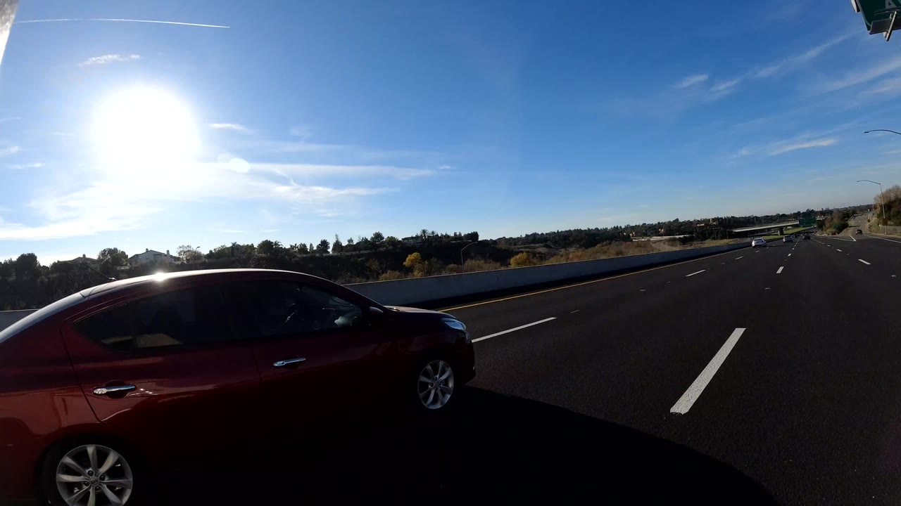 Red car beside freeway lanes in strong sunlight