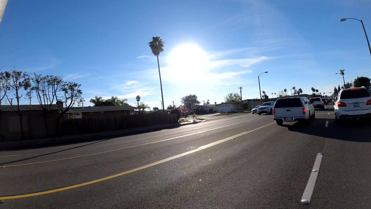 White pickup and SUVs in sunlit traffic on a broad road.