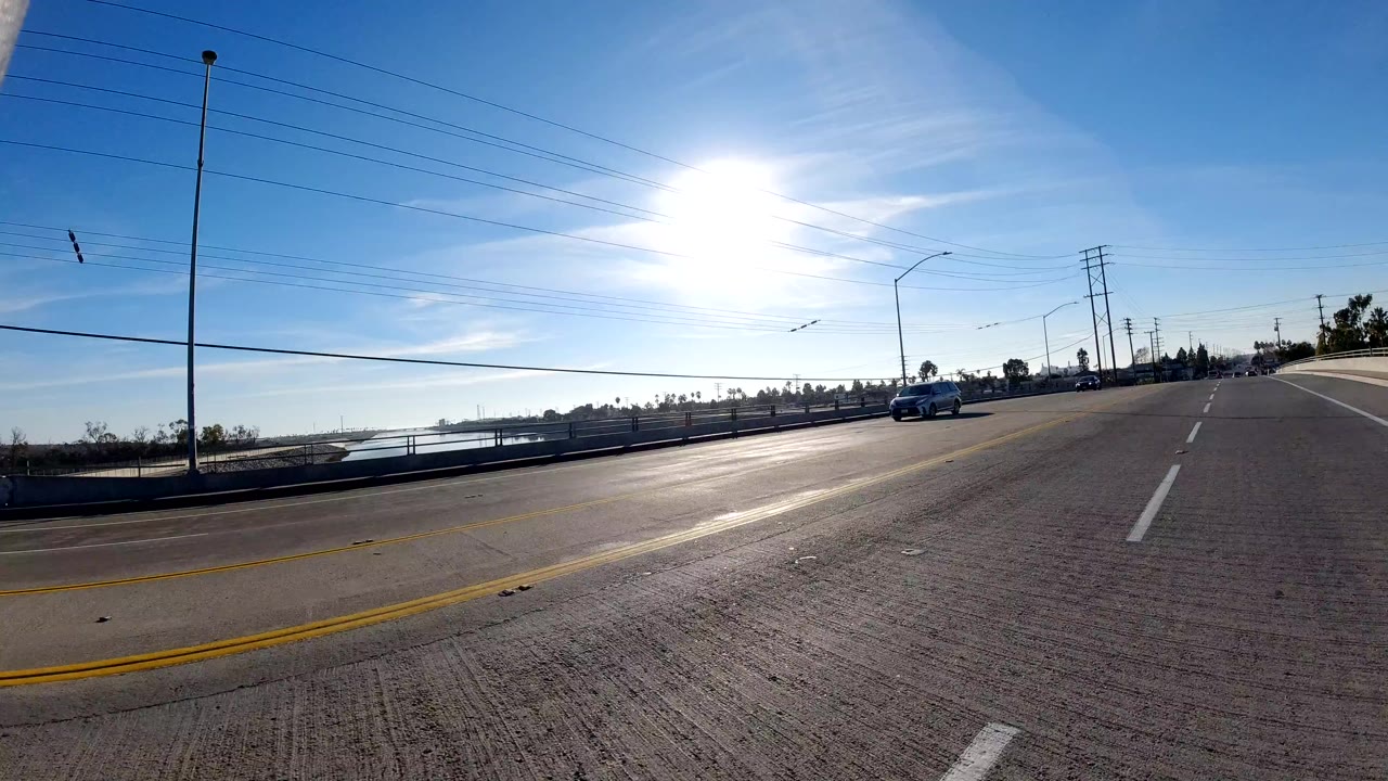 Wide road-level view in Orange, California with bright sun glare, lane markings, distant cars, utility lines, and no visible people.