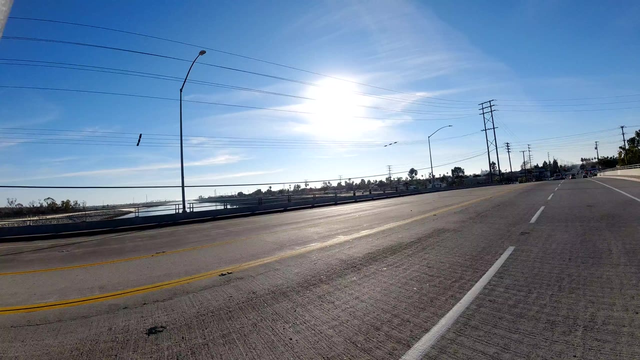 Sunlit multi-lane road with distant cars, utility poles, and low roadside buildings.