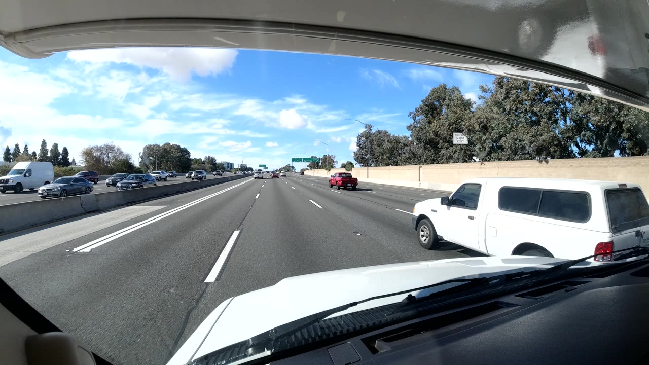Freeway traffic seen through a windshield with a white van passing on the right.