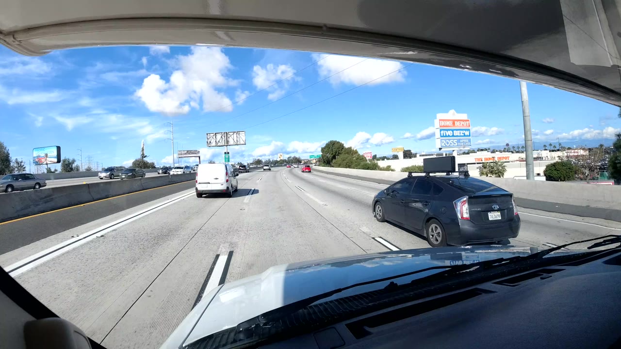 Highway lanes seen from a dashboard with a white van ahead and billboard signs to the right.