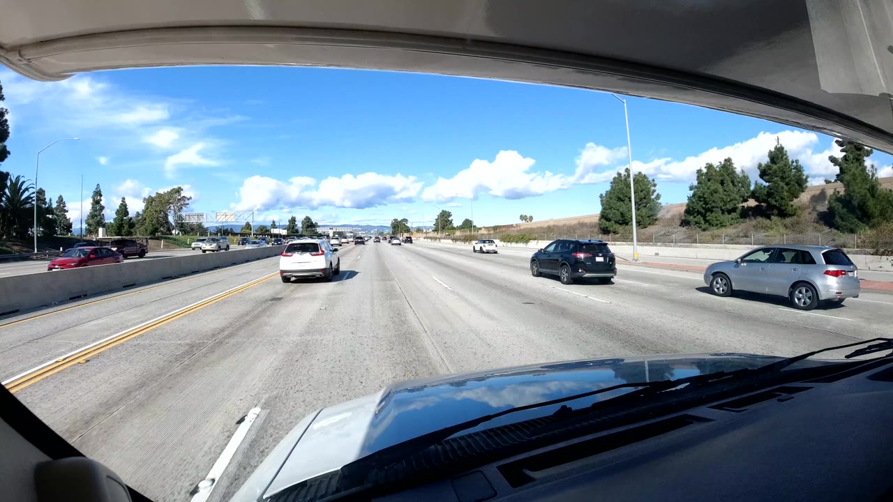 Open freeway lanes with cars ahead and a long sound wall.